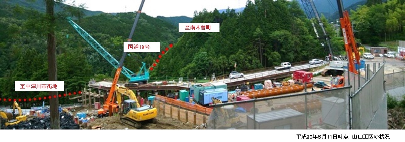 工事現場の写真で複数のクレーンやショベルカーと資材が並び山間の道路沿いに車両が停まっている様子を上空から撮影した画像平成30年6月11日時点