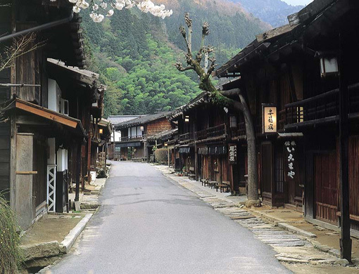 古い木造の商家が両側に並ぶ静かな山間の通りの風景で中央に歩行者はいない