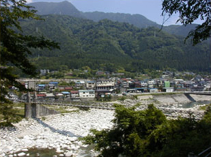 山あいの集落の手前を白い川が流れアーチ状の橋が架かる風景写真