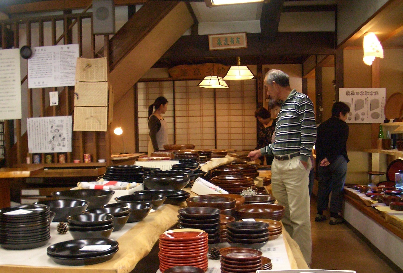 漆器や皿が並ぶ店内で横縞のシャツを着た男性が商品を手に取り選んでいる様子