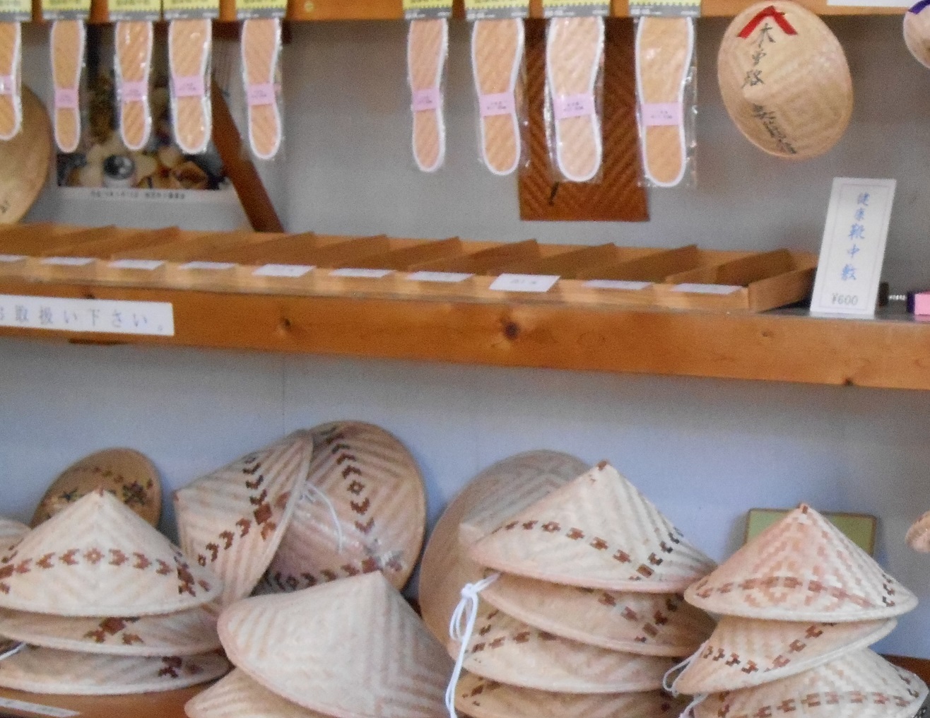 白い花柄の皿やボウルが棚に積まれ上部の木製棚に包丁や木の器具が掛けられたキッチン用品の陳列