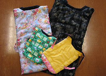 木目の上に花柄やアヒル柄や無地のカラフルな布製マスクやポーチが重なっている写真