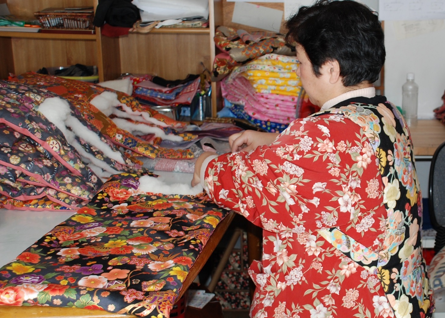 ミシンで色とりどりの花柄布地を縫う人物の横顔がぼかされている作業風景