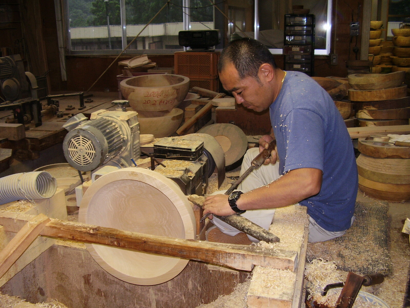 工房の作業台で木製の円盤を旋盤で削る作業者が道具を持って加工している様子