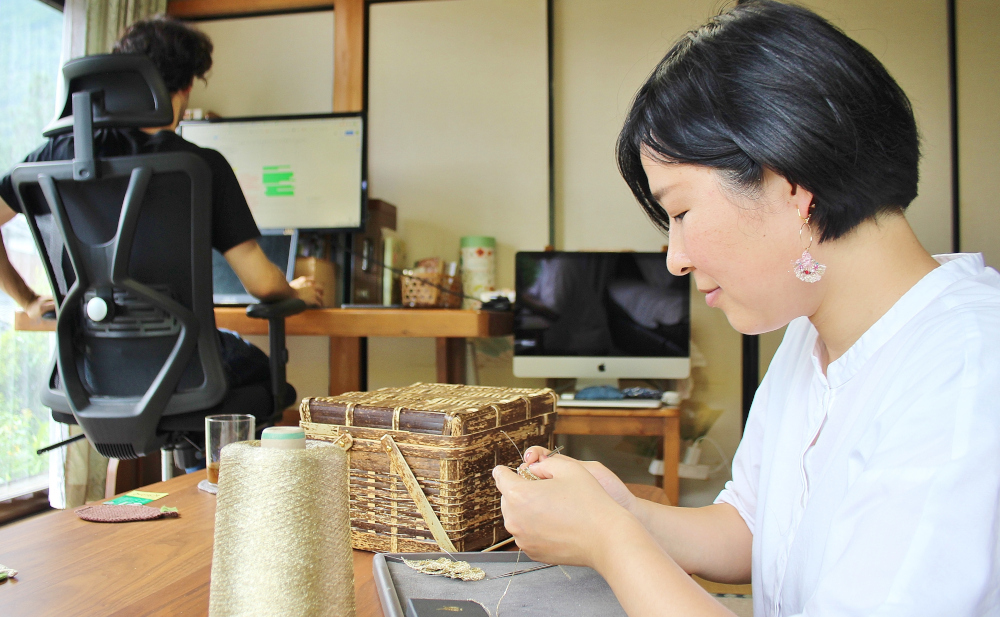 作業机の上に糸巻きと編みかけの柳かごが置かれ手作業で編み物をする風景