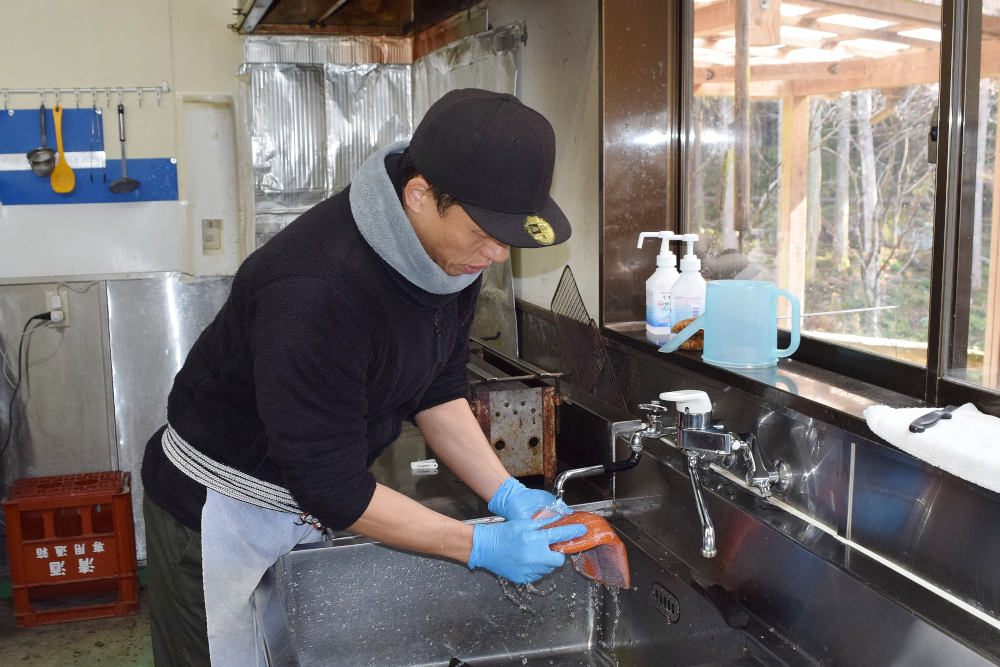 手袋をはめた人が厨房の流しで魚を洗っている