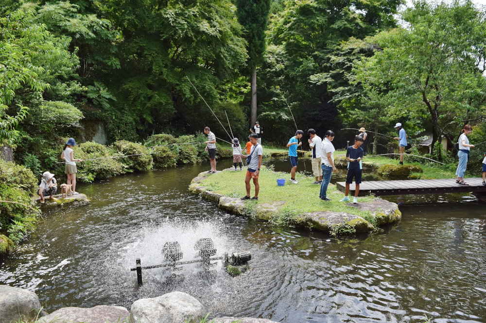 緑豊かな公園の池の周りで子どもや大人が散策したり写真を撮ったりしている風景