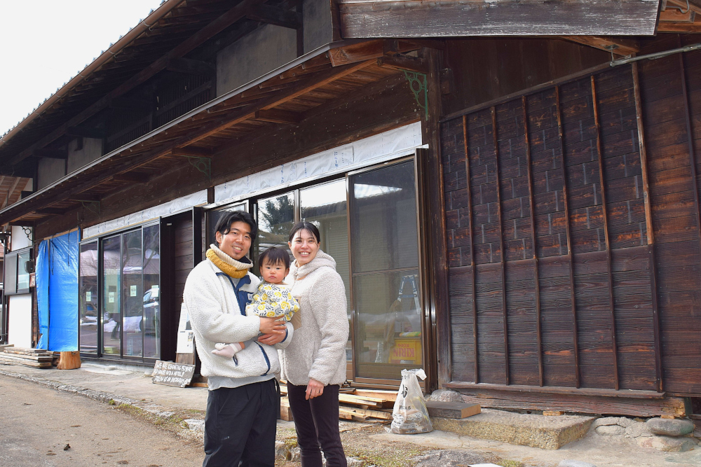 大人二人が子どもを抱いて古い木造の店舗の前に立っている