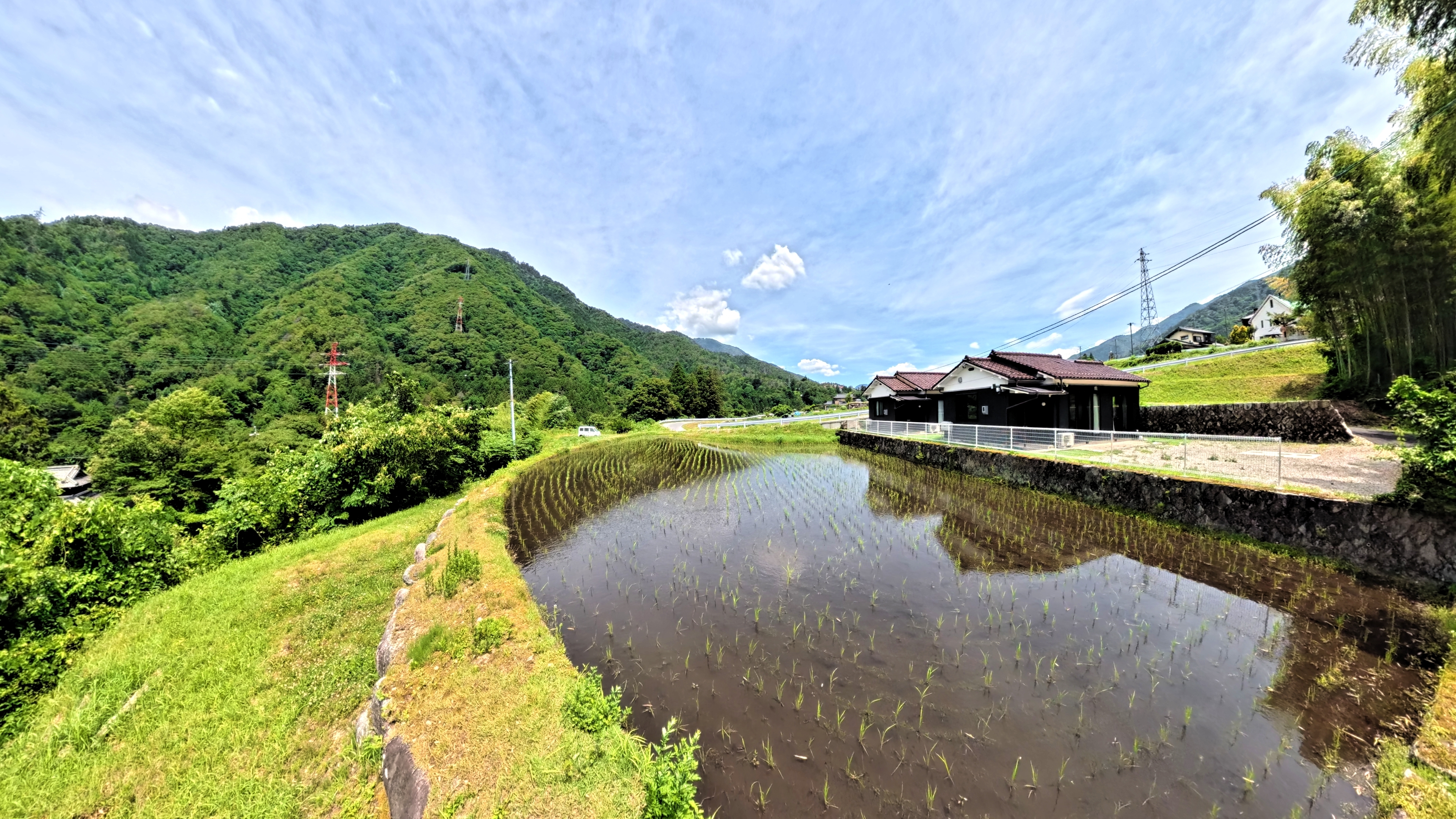 山あいの集落と水を張った田んぼに映る家屋と青空が広がる風景