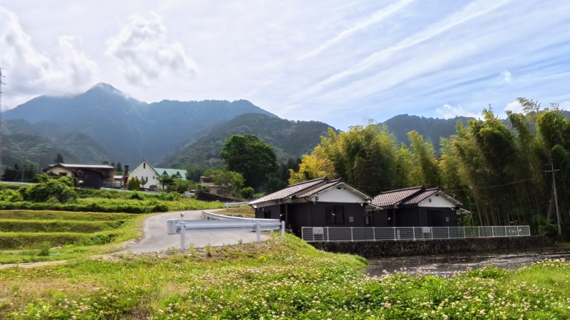 山を背景に田んぼと川沿いの住宅と白い欄干の橋がある風景
