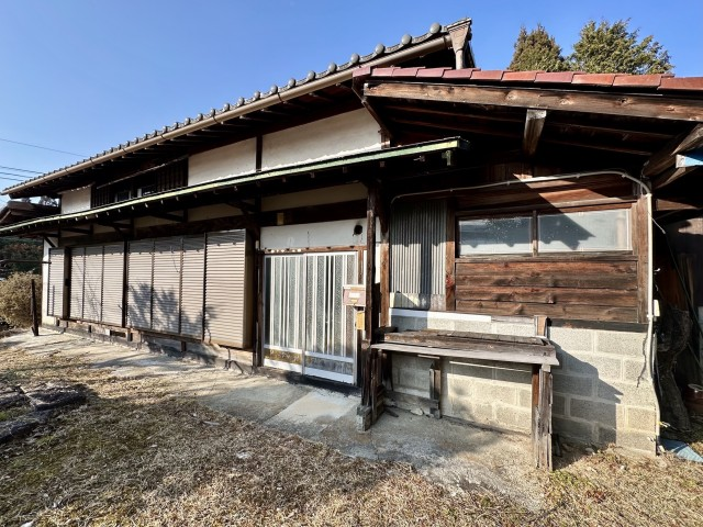 古い木造の日本家屋がシャッターと引き戸で閉ざされた正面と空の見える庭に面している