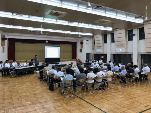 会議室で参加者が集まり、プレゼンテーションを聞いている様子。