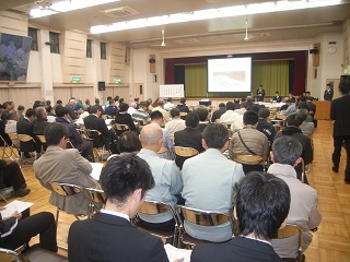 多くの人々が集まっている講演会の様子。